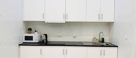 A compact kitchen with white cabinets, a microwave, a kettle, and a sink.