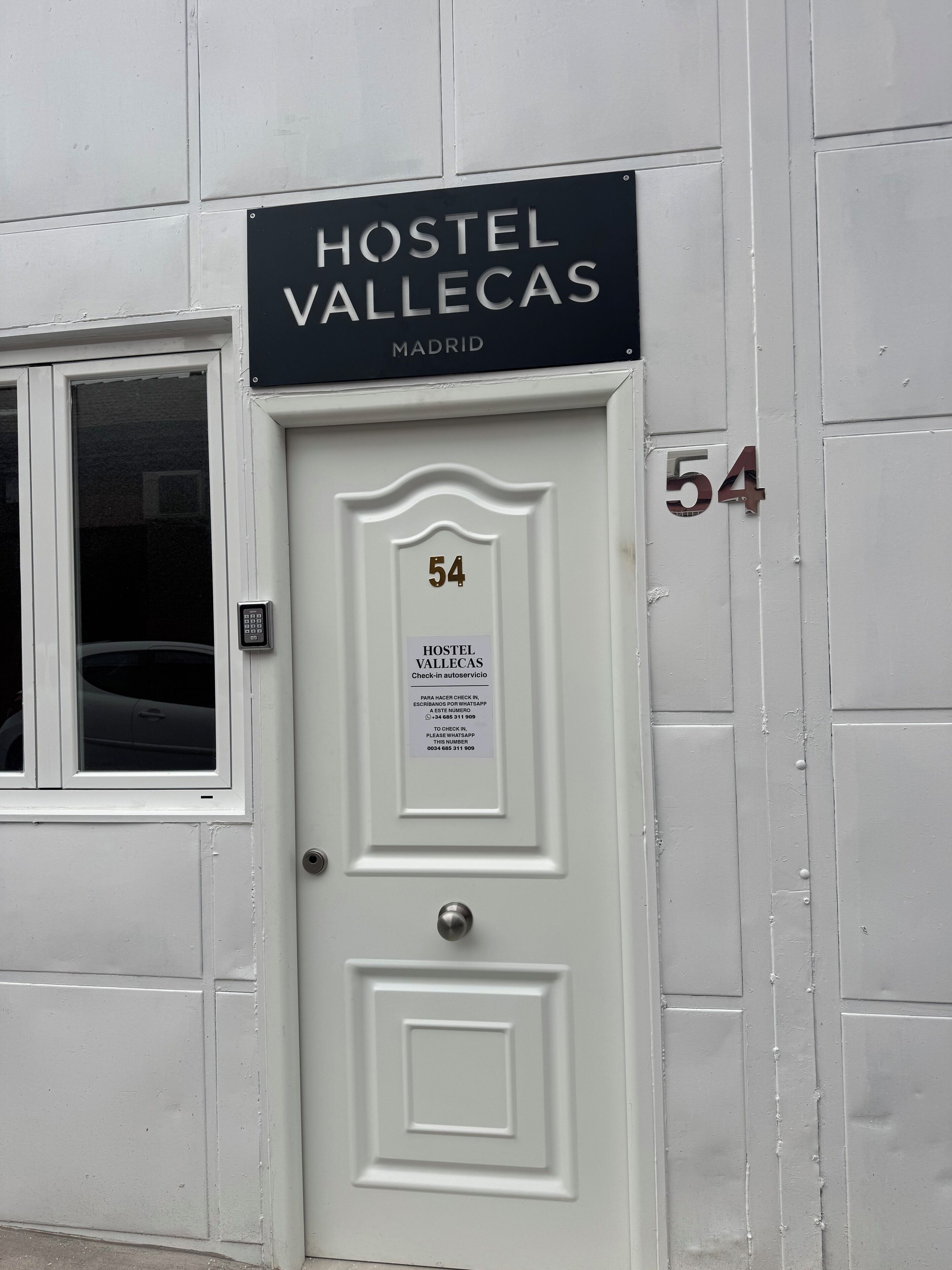 A white door with a sign above it that reads "HOSTEL VALLECAS MADRID" and the number "54".