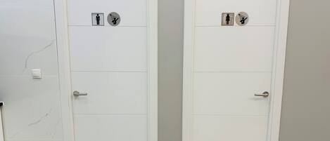 Two white doors with gender-specific symbols and a hand symbol, indicating restrooms.