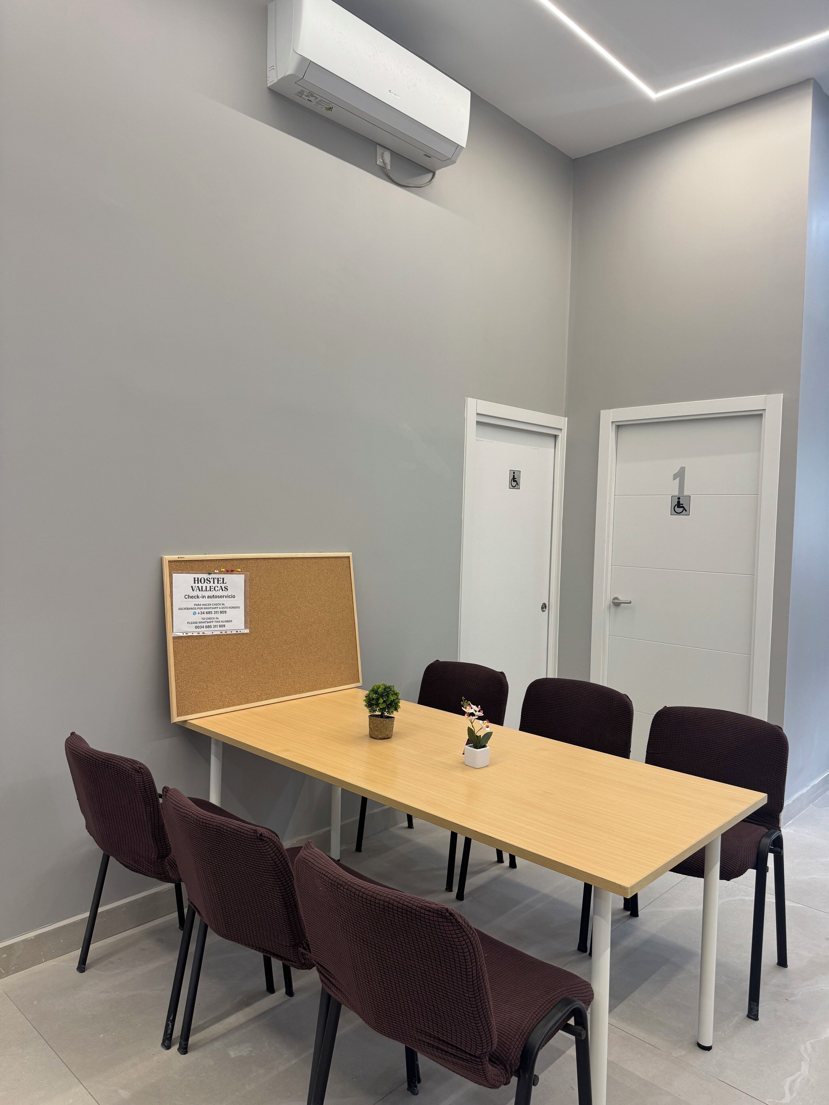 A conference room with a long table, six chairs, a potted plant, and a bulletin board with a sign.