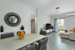 Una sala de estar moderna con un televisor de pantalla plana, un comedor con un bol de fruta y un espejo grande en la pared.