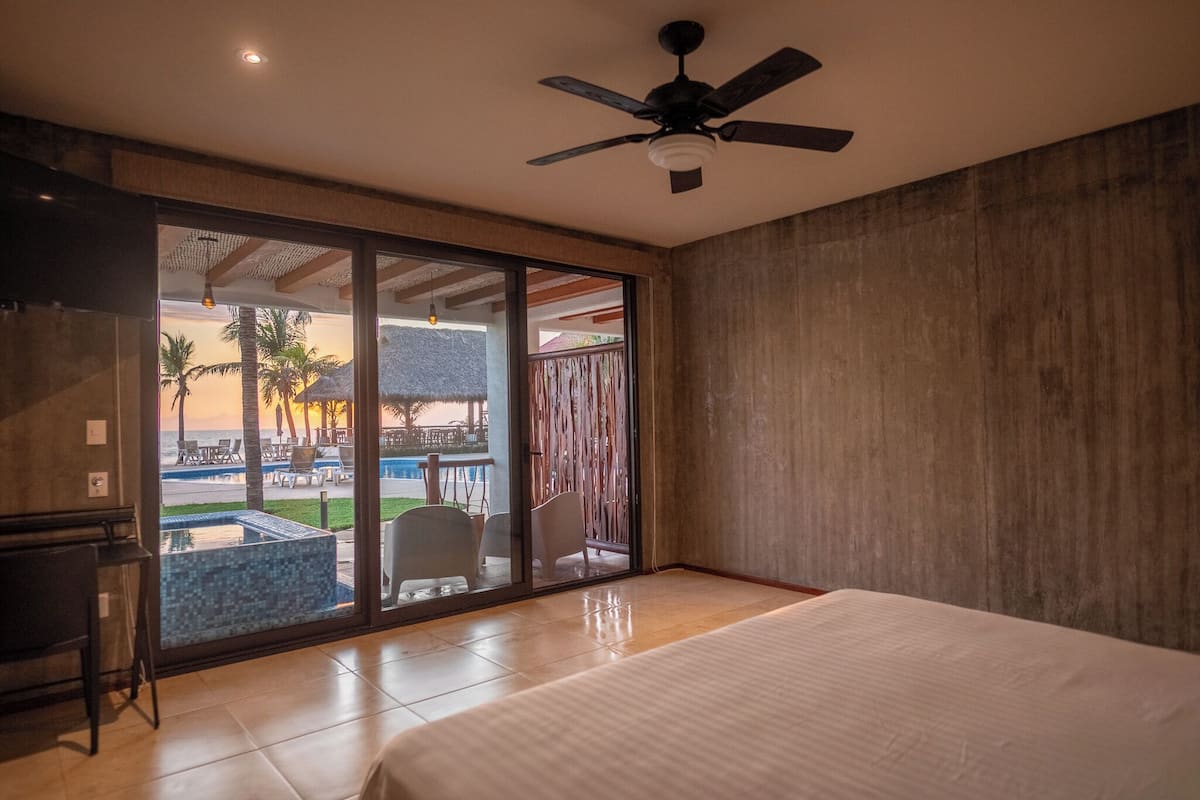 A bedroom with a large bed, a ceiling fan, and a sliding glass door leading to a pool area with outdoor seating.