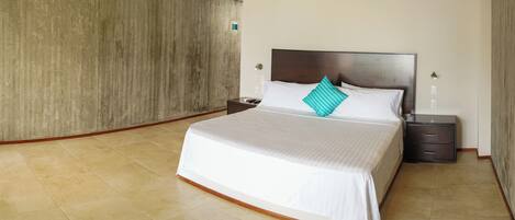 A hotel room with a large bed, a nightstand, a drawer, and a concrete wall.