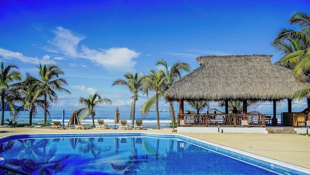 A swimming pool with clear blue water, surrounded by palm trees and a thatched-roof structure. - Portofino Hotel & Restaurante (Barra de Potosi)