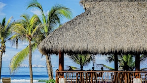 A thatched-roof structure with a wooden railing, palm trees, and a view of the ocean. - Portofino Hotel & Restaurante (Barra de Potosi)