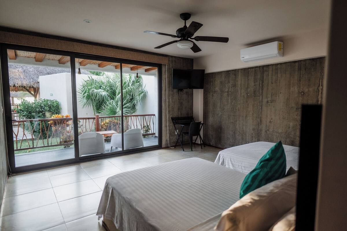 A hotel room with two beds, a ceiling fan, a TV, and a balcony with a table and chairs.
