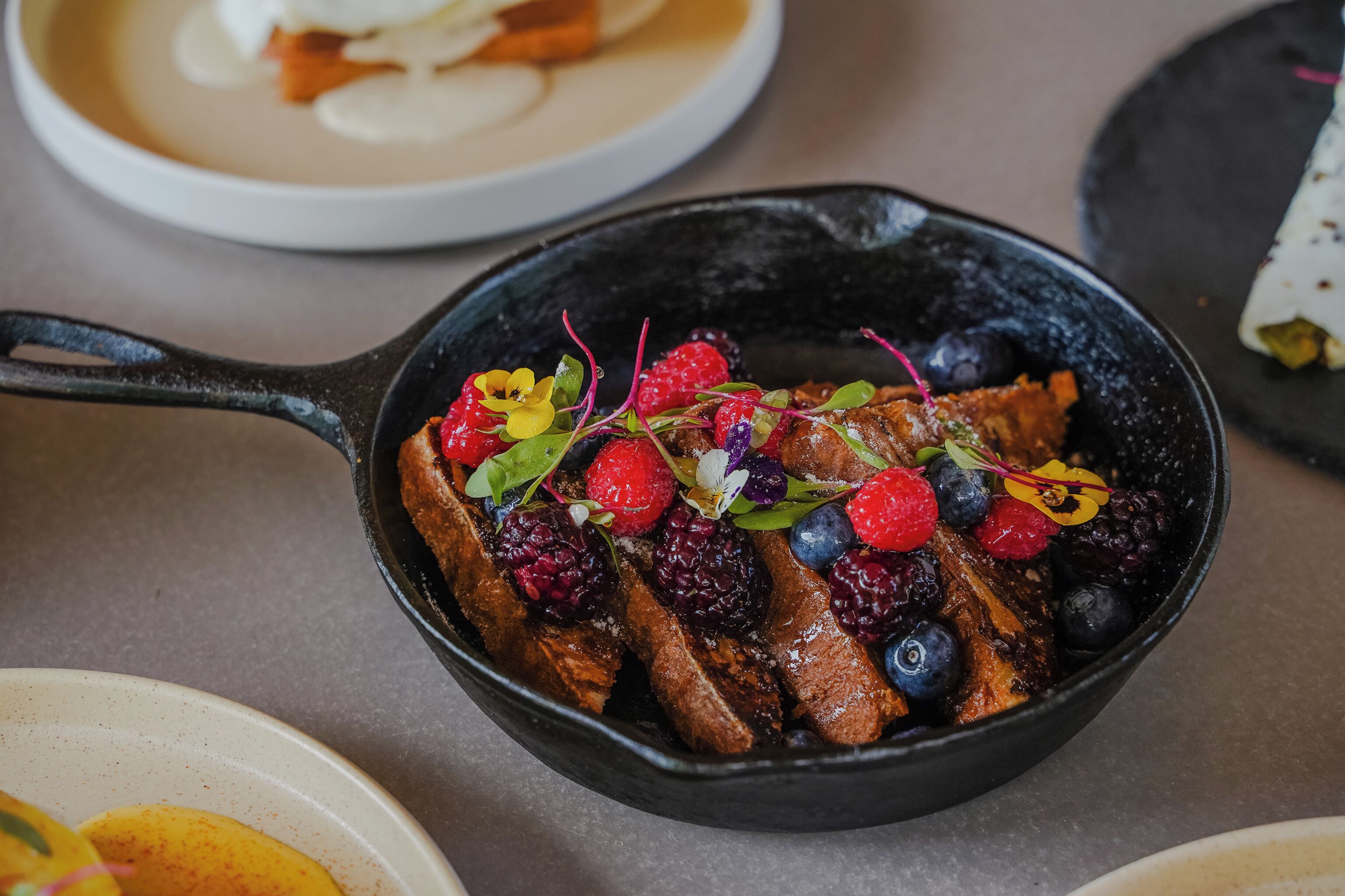 A skillet with French toast topped with berries and greens.