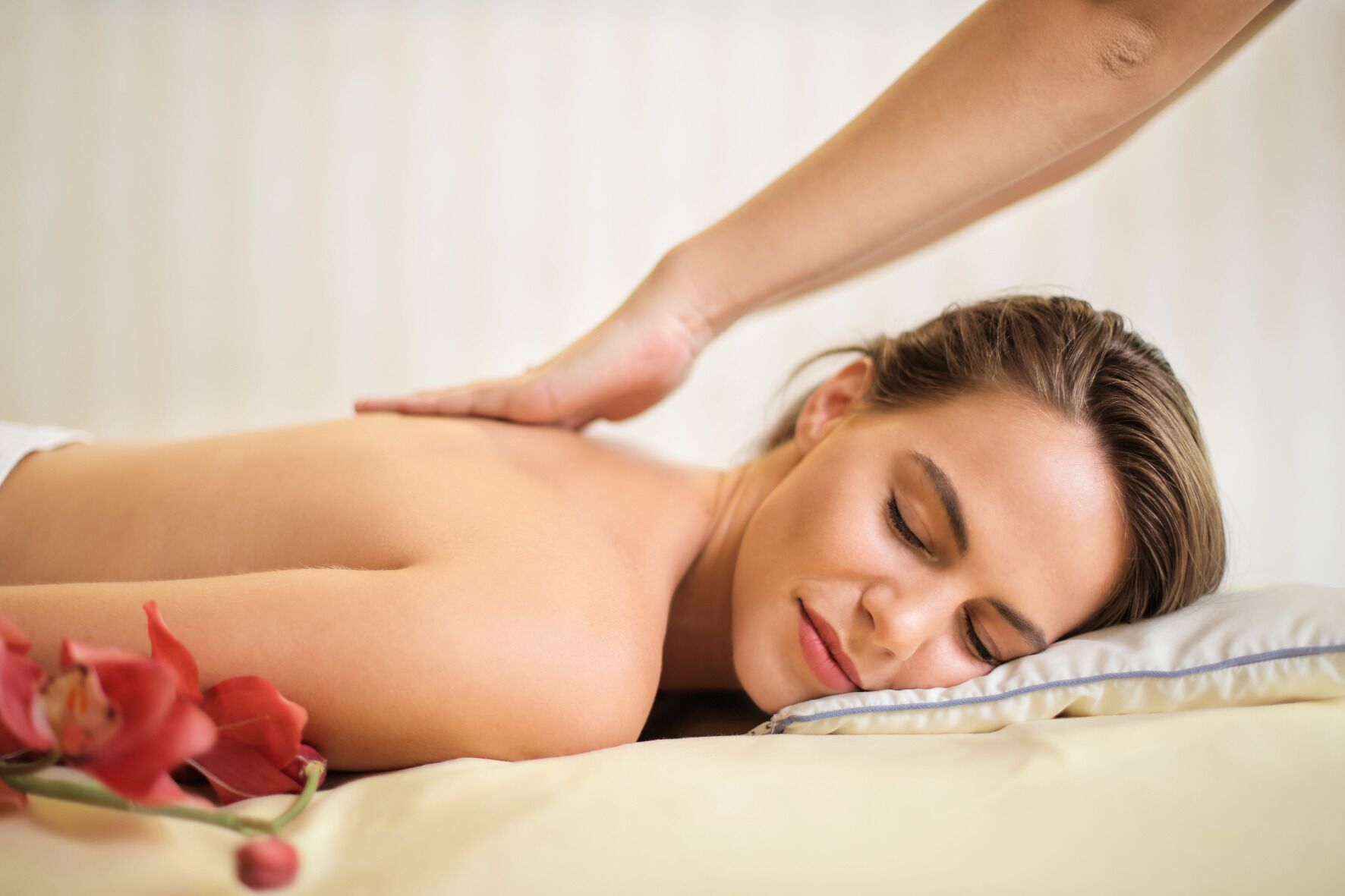 A person receiving a back massage in a room with a bed and a pillow.