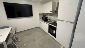 Una cucina compatta con una TV a schermo piatto fissata al muro, un forno a microonde, una macchina per il caffè e un frigorifero.