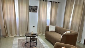 Una sala de estar con un sofá marrón, un sillón marrón más pequeño, una mesa redonda de centro y una alfombra estampada.