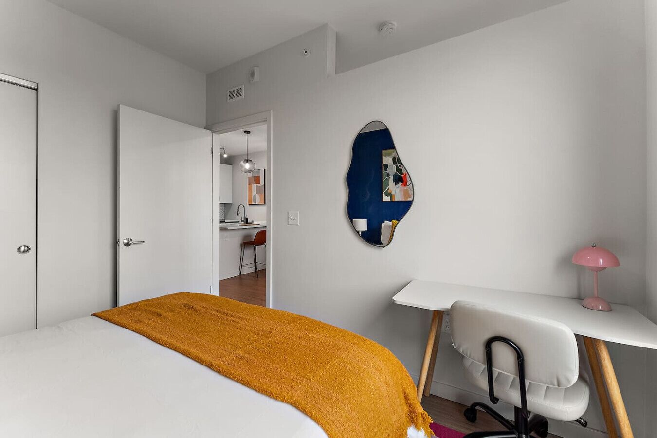 A modern bedroom with a bed, a desk, a chair, and a mirror on the wall.