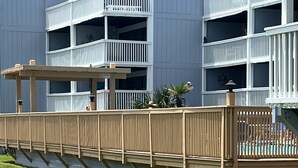A multi-story building with a wooden deck and a fenced pool area.