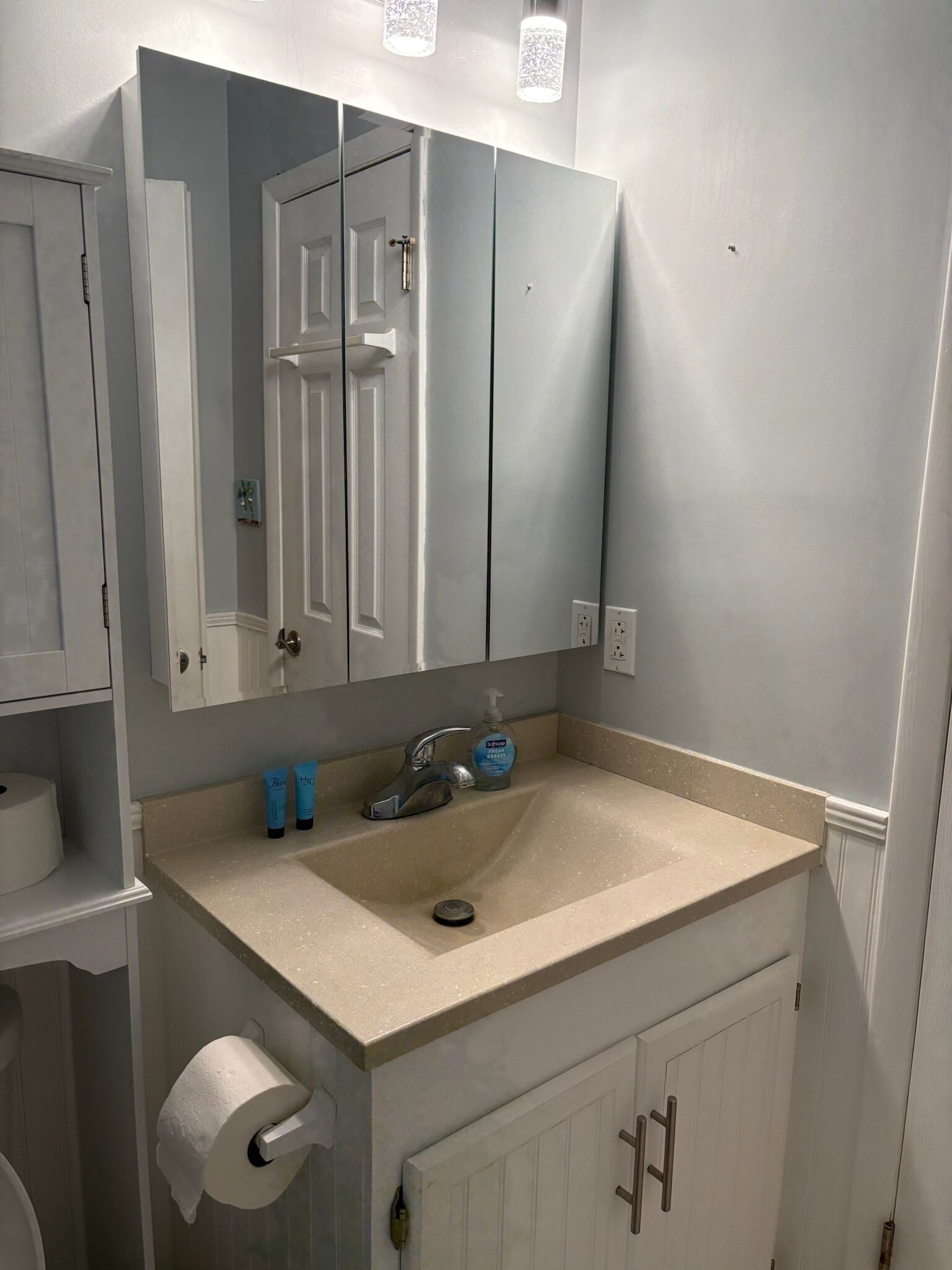 A bathroom with a sink, mirror, and toilet paper.