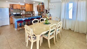 A spacious kitchen with wooden cabinets, a central island with stools, and a dining table with chairs.