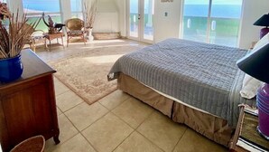 A spacious bedroom with a large bed, a ceiling fan, and a view of the ocean through the sliding glass doors.