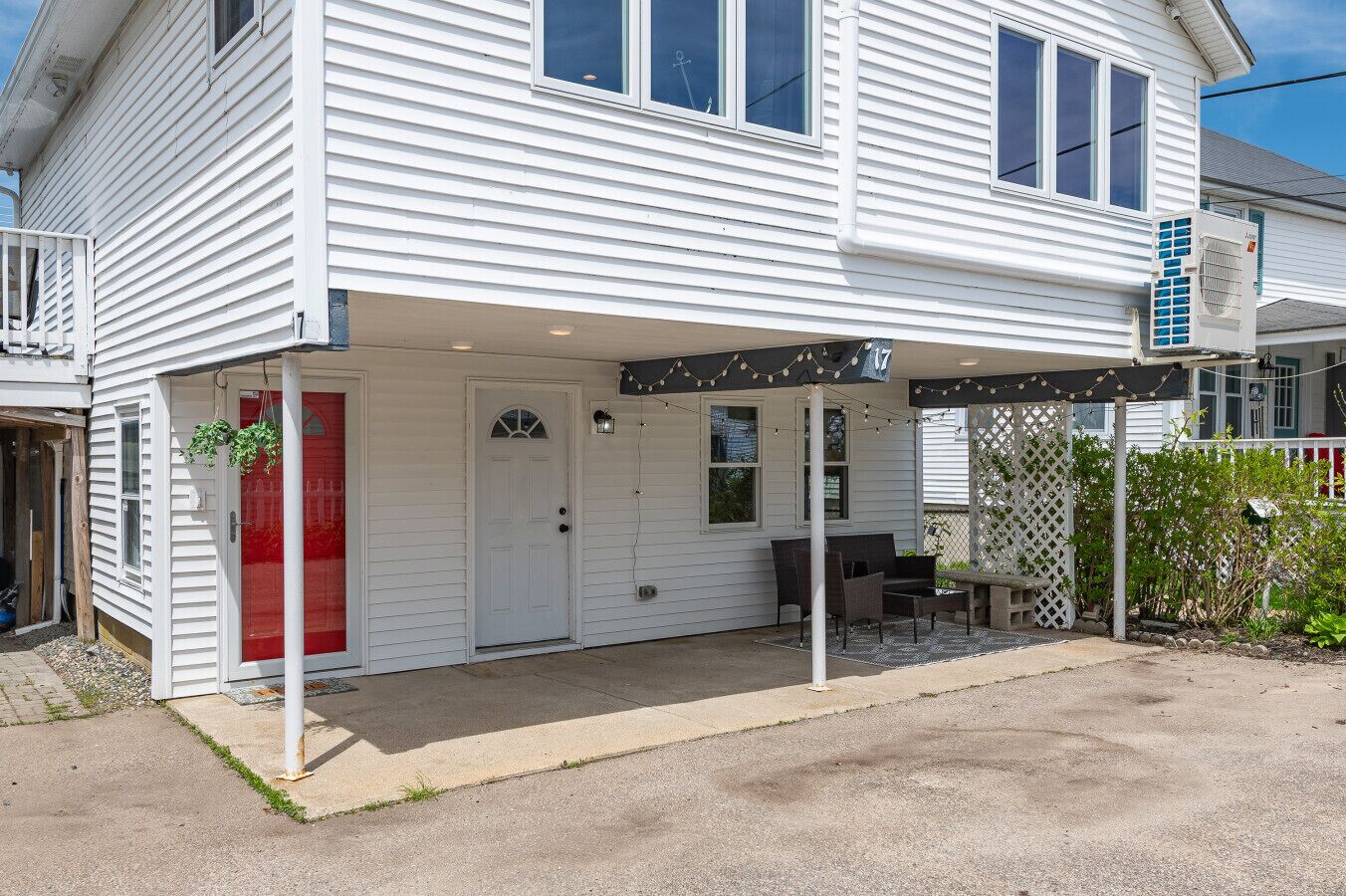 A white two-story house with a covered porch, a red door, and a small outdoor seating area.