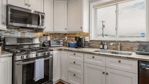 A modern kitchen with white cabinets, a stainless steel stove, a microwave, a toaster, and a large window. - Hampton Beach, Free Parking, Sunsets (Hampton)