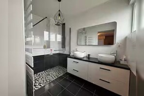 Une salle de bain moderne avec un grand miroir, un lavabo blanc et un sol carrelé de couleur noire.