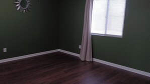 A room with green walls, a dark wooden floor, and a window with blinds. - Charming 1-bedroom house in Riverside (Riverside)