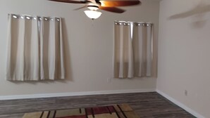 A room with a ceiling fan, two windows with curtains, a wooden floor, and a partial view of a rug. - Charming 1-bedroom house in Riverside (Riverside)