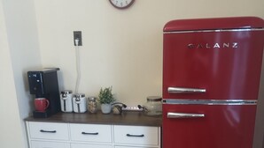 Eine Küche mit einem roten Galanz-Kühlschrank, weißen Schränken, einer Kaffeemaschine und einer Wanduhr.