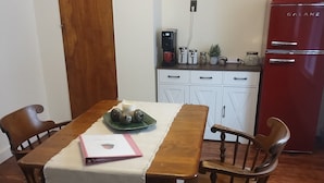 Ein Essbereich mit Holztisch und Stühlen, einer weißen Tischdecke, einer Uhr an der Wand und einem roten Kühlschrank im Hintergrund.