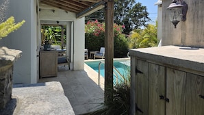 Un patio techado con piscina, muebles de madera y una pared de piedra.