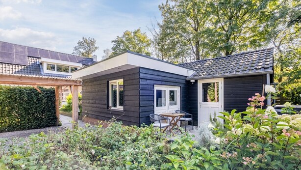 Ein modernes Haus mit dunkler Fassade, einer kleinen Terrasse mit Tisch und Stühlen sowie einem Garten mit verschiedenen Pflanzen.