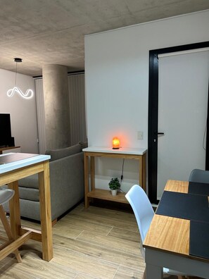 A modern living space with a wooden dining table, a sofa, and a small desk with a heater. - Hestia at Icon Boulevard Caseros (Buenos Aires)