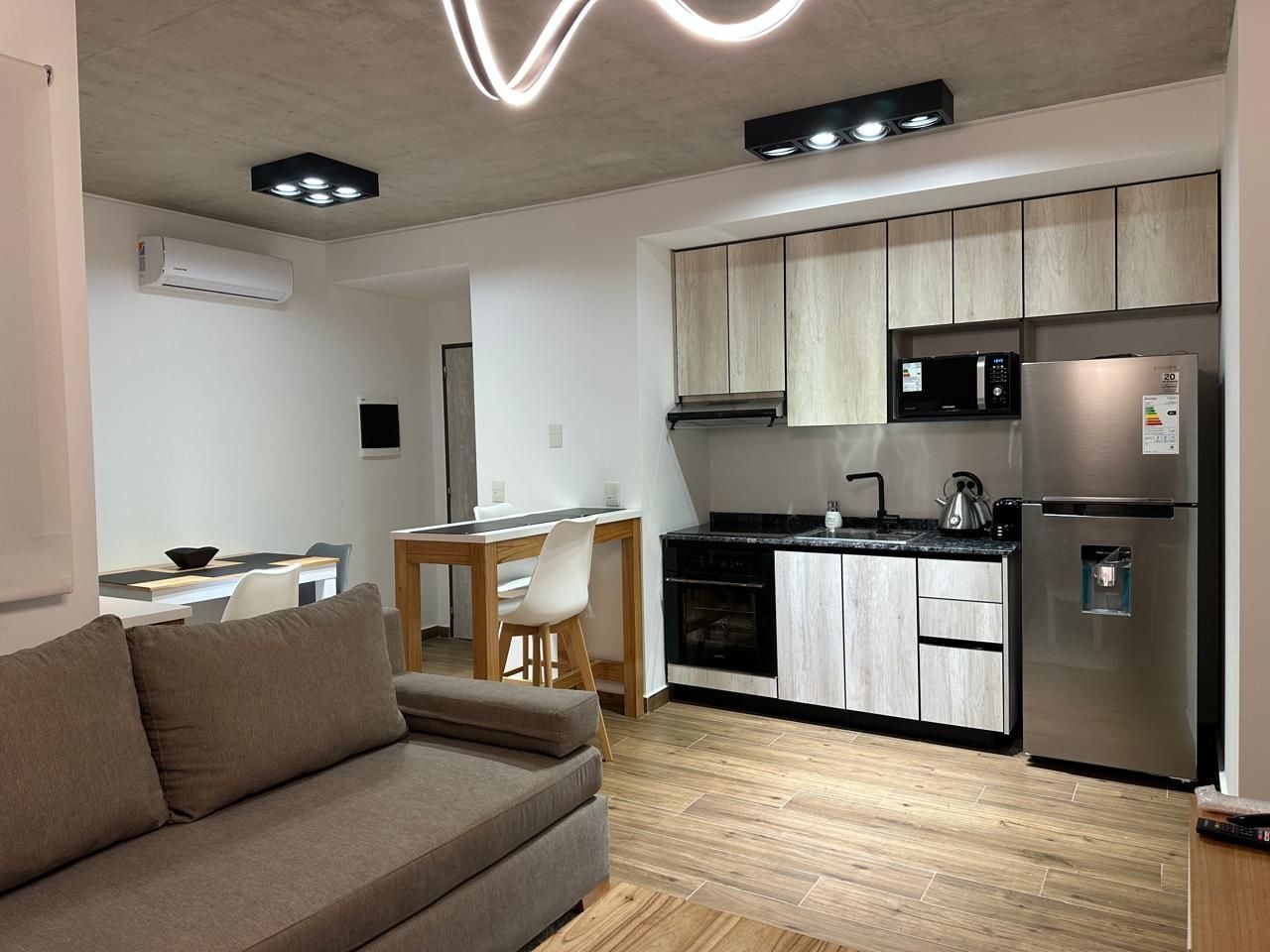 Cocina moderna equipada con refrigerador, microondas y estufa. Cuenta con un comedor con mesa y sillas.