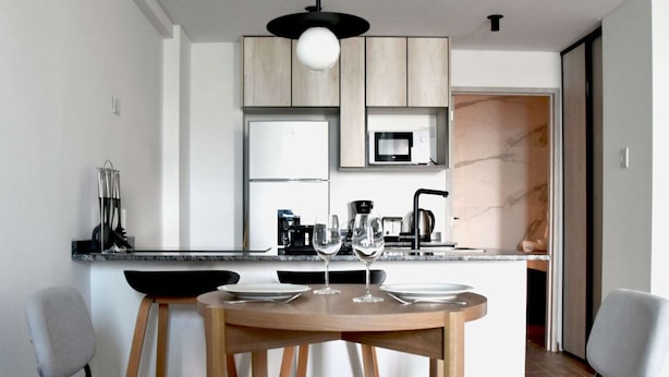 A modern kitchen with wooden cabinets, a built-in microwave, and a round dining table with chairs. - Hestia at Icon Boulevard Caseros (Buenos Aires)