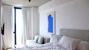 A hotel room with a bed, a sofa, a large window with curtains, and a wall-mounted artwork. - Hestia at Icon Boulevard Caseros (Buenos Aires)