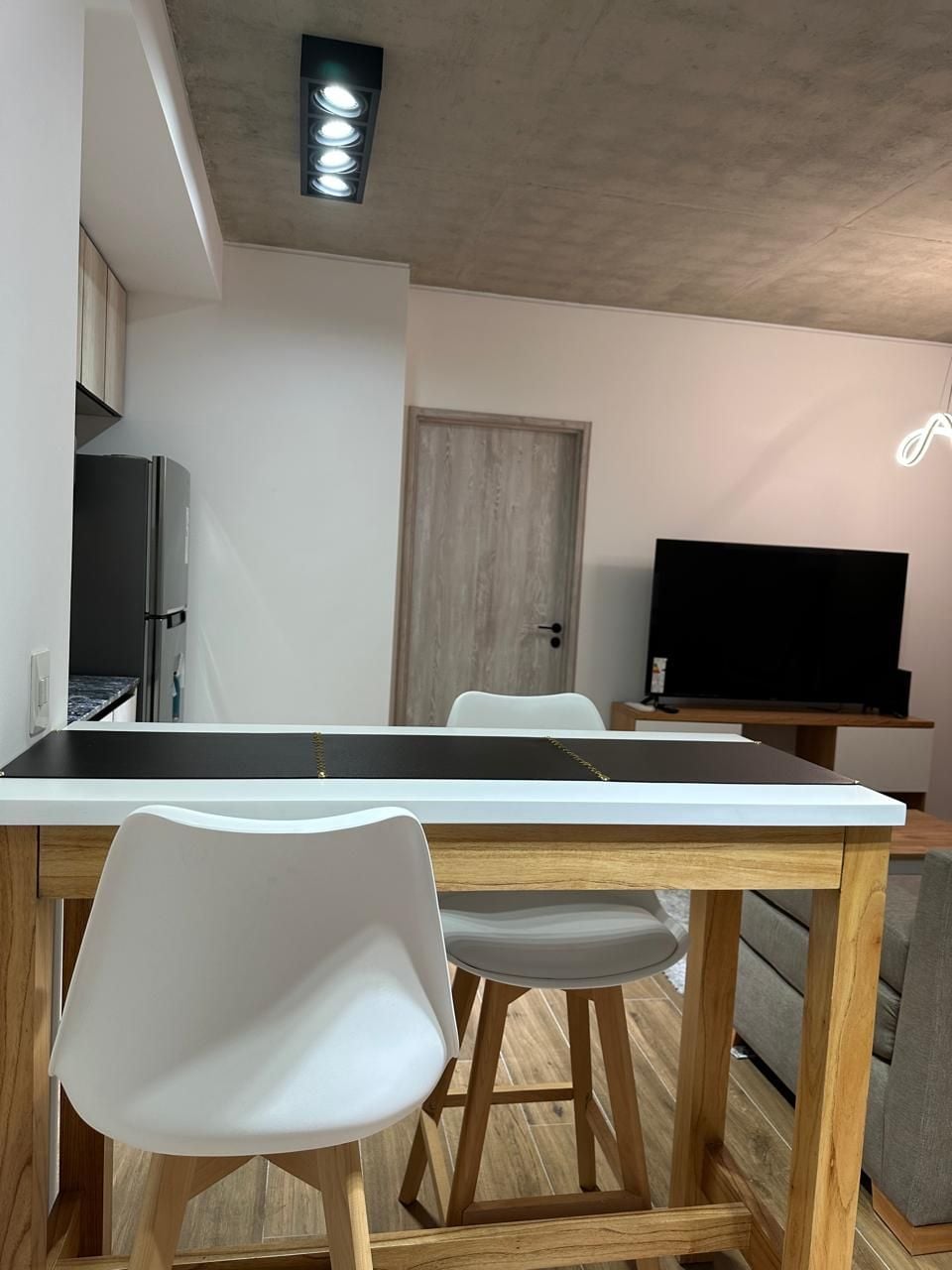 A dining area with a wooden table, white chairs, a television, and a door in the background.