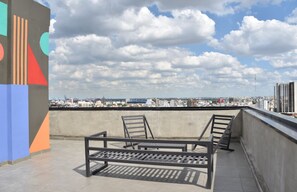 A rooftop terrace with a view of the city skyline, featuring a concrete wall and metal chairs. - Hestia at Icon Boulevard Caseros (Buenos Aires)