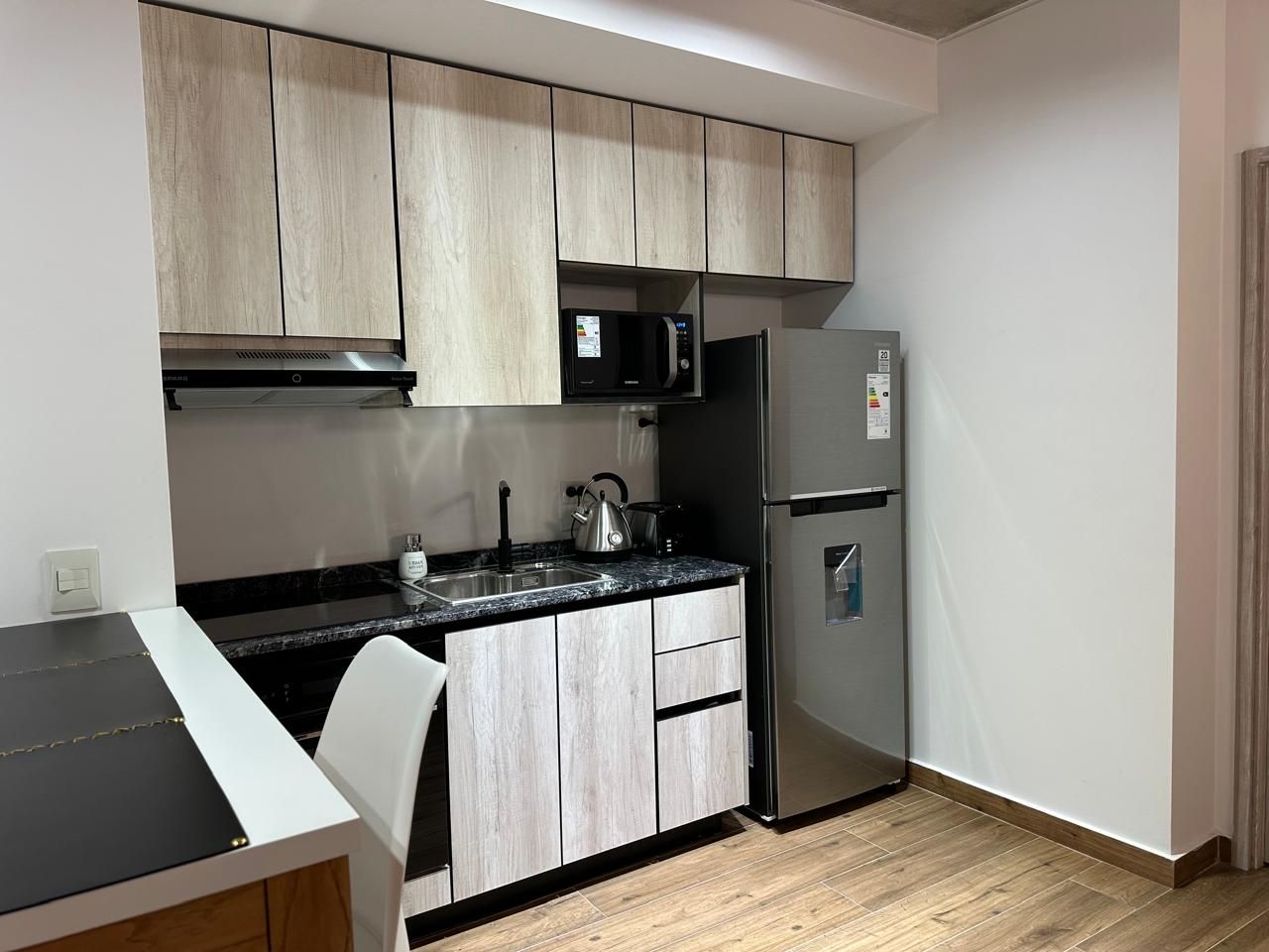 A compact kitchen with a microwave, refrigerator, and a kettle on the countertop.