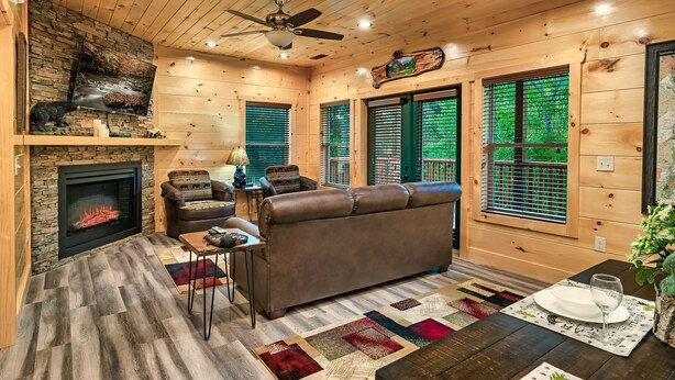 A cozy cabin interior with a fireplace, leather sofa, wooden flooring, and large windows. - HUGE Heated Indoor Pool, 2 King Beds, A+ Location, Arcade (Sevierville)