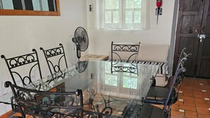 A dining area with a glass table surrounded by black metal chairs, a fan, and a window with curtains. - MEXICAN HOUSE WITH LOVE (San Sebastián del Oeste)