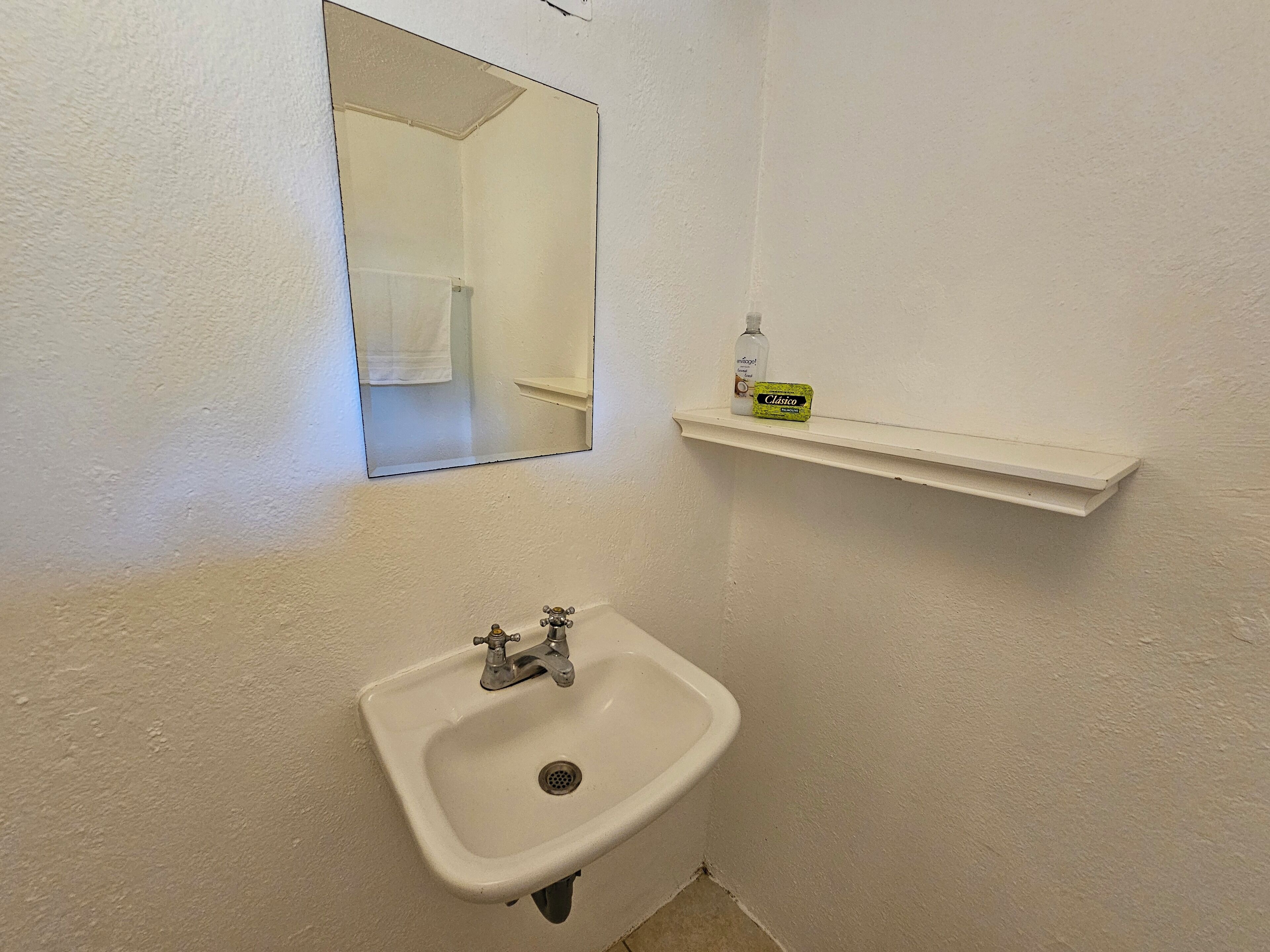 Une salle de bain avec un lavabo blanc, un miroir et une étagère contenant des articles de toilette.