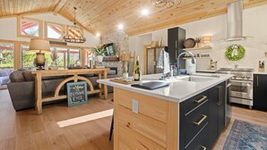 A modern kitchen with a central island, wooden ceiling, and a stone wall. - Chardonnay Chalet - A Modern Mountain Getaway (Blowing Rock)