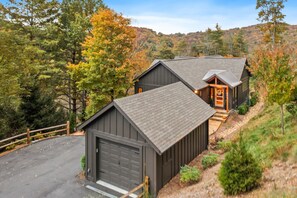 Eine Holzhütte mit Garage und kleiner Veranda, umgeben von Bäumen und einer hügeligen Landschaft.