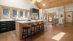 A modern kitchen with a central island, bar stools, and a chandelier. - Chardonnay Chalet - A Modern Mountain Getaway (Blowing Rock)