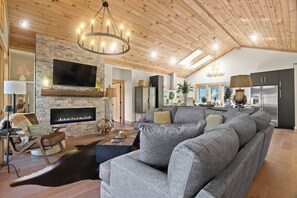 Ein modernes Wohnzimmer mit Kamin, einem großen grauen Sofa und einer Holzbalkendecke.