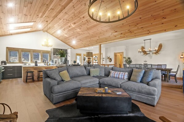 A spacious living area with a large gray sectional sofa, a wooden coffee table, and a kitchen in the background.