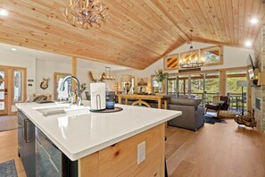 Une cuisine spacieuse dotée d’un grand îlot central, d’un plafond en bois et d’un coin repas offrant une vue agréable.