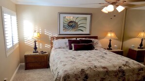Une chambre à coucher comprenant un lit, deux tables de chevet, une commode, un grand miroir et un ventilateur de plafond.