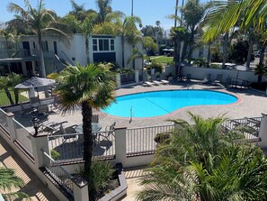 A swimming pool surrounded by palm trees and lounge chairs, with a building in the background.