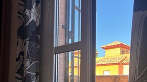 A view through a window with a metal gate, a brick wall, and a yellow building with a tiled roof.