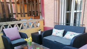 An outdoor seating area with wicker furniture, a glass coffee table, and a potted plant.