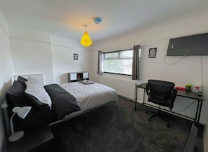 A hotel room with a bed, desk, chair, and a window with blinds.