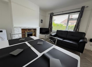 Un salon moderne avec une cheminée, un canapé en cuir noir, une table à manger avec des sets de table noirs et un téléviseur.